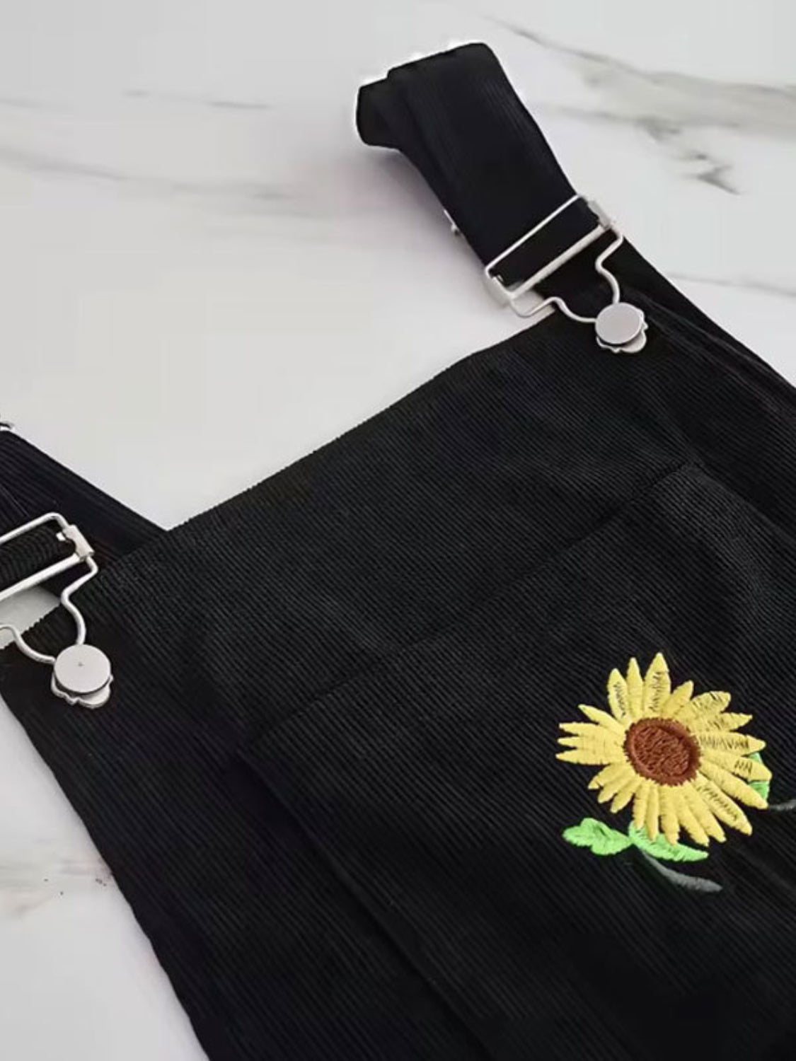 Black corduroy overalls with embroidered sunflower detail and silver hardware.