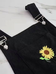 Black corduroy overalls with embroidered sunflower detail and silver hardware.