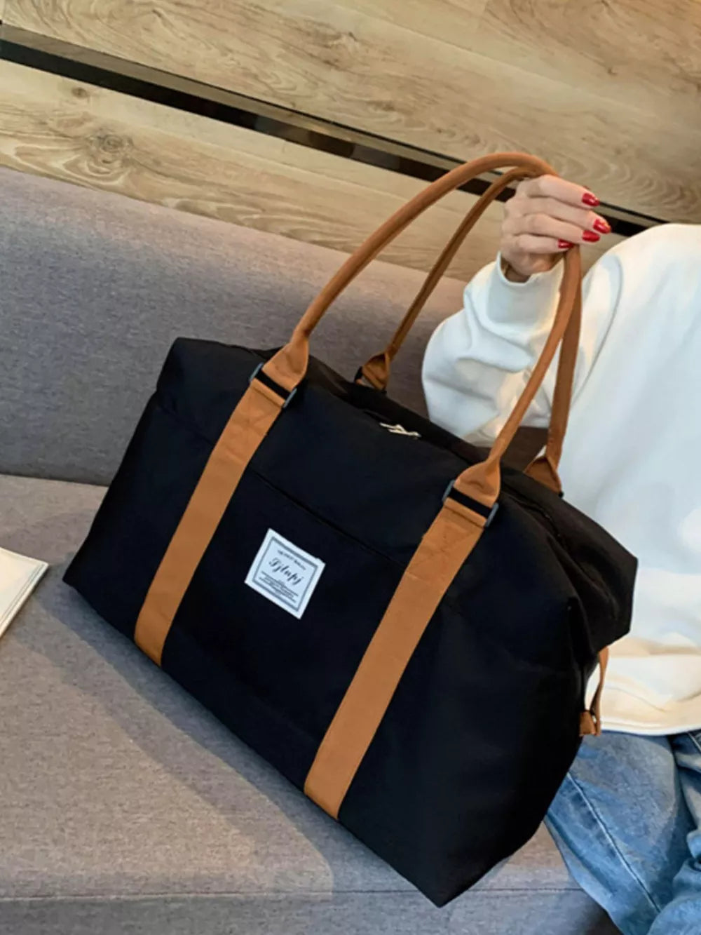 Large black Oxford cloth travel bag with tan contrast straps and handles.