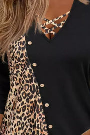 Black blouse with leopard print panel, crisscross neckline, and button detail.