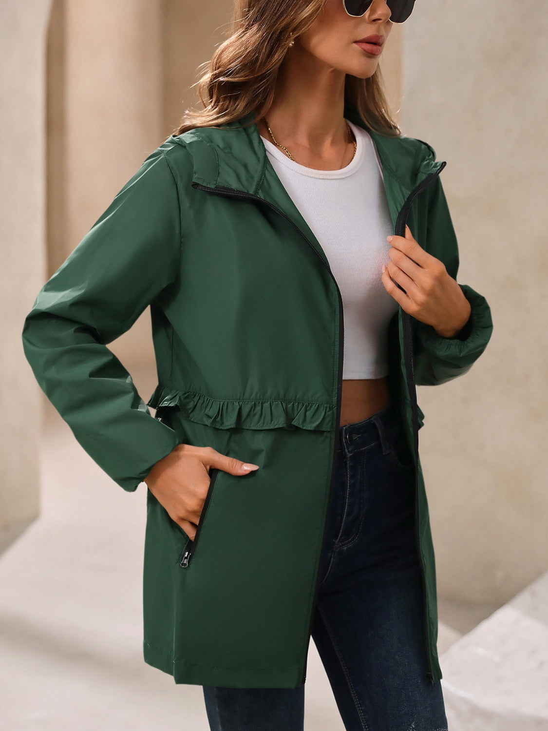 Dark green hooded windbreaker jacket with ruffled waistline and zippered pockets.