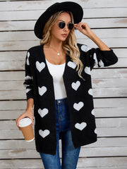 Black acrylic cardigan with white heart intarsia pattern, open front, long sleeves.