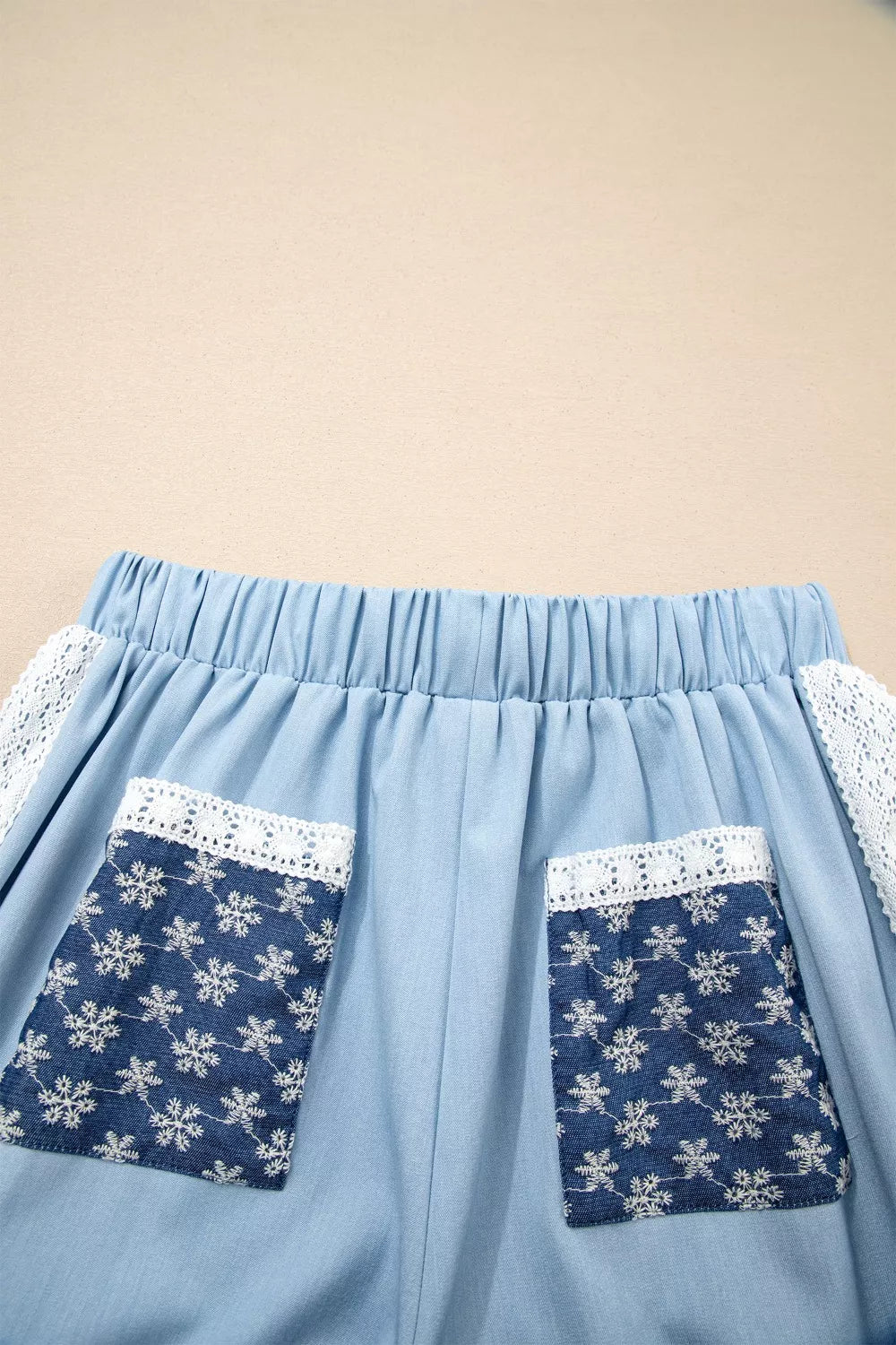 Light blue maternity pants with elastic waist, lace trim, and snowflake-patterned pockets.