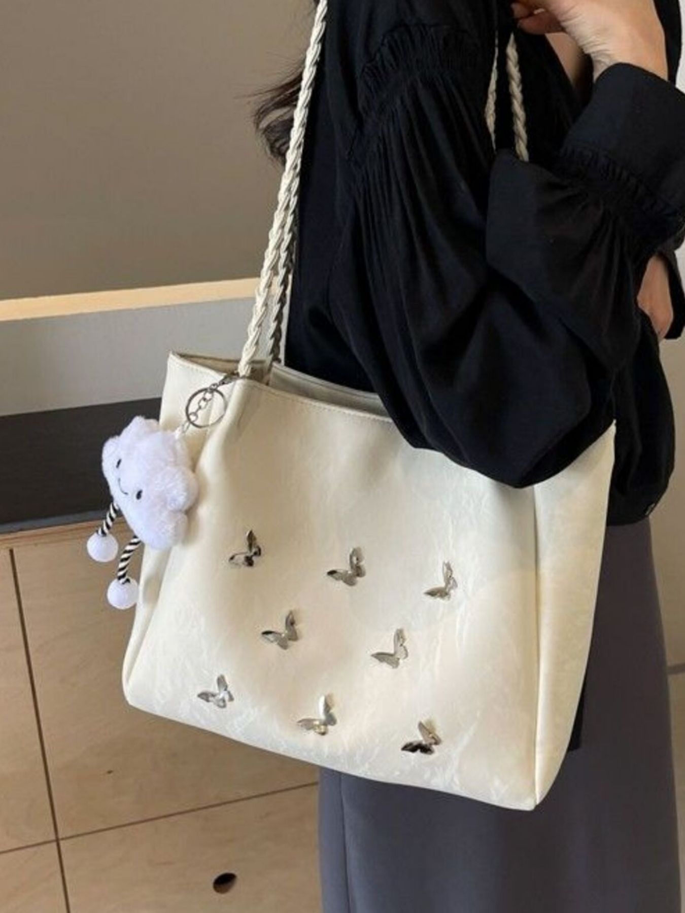 Cream shopper bag with braided handles, butterfly embellishments, and cloud charm.