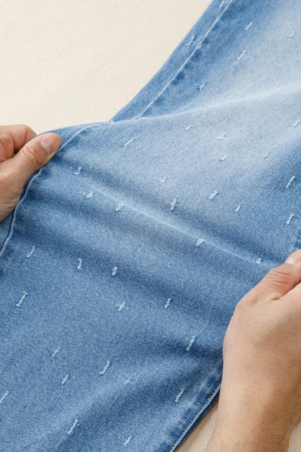 Light wash denim jeans with distressed details and a raw hem.