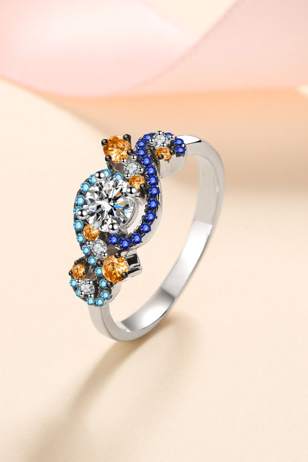 Silver ring with a central clear gem and swirling accents of blue, orange, and clear small gems.