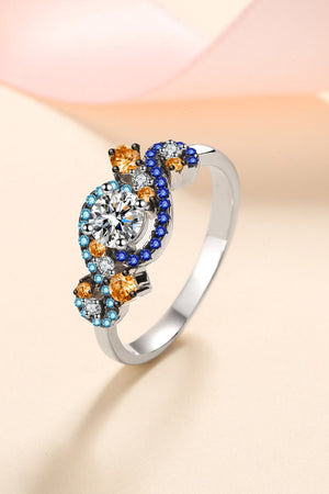 Silver ring with a central clear gem and swirling accents of blue, orange, and clear small gems.