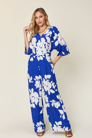 Cobalt blue floral kimono jumpsuit with wrap V-neck, wide sleeves, and wide-leg pants.