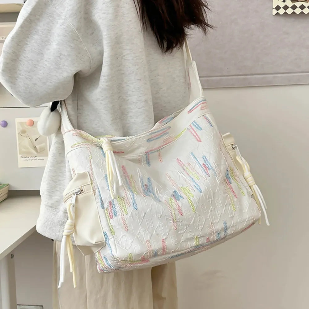 White slouchy shoulder bag with colorful embroidered lines and tassel details.