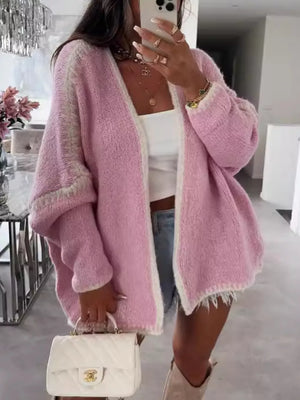 Oversized pink cardigan with contrast trim and frayed hem, worn open over a white top.