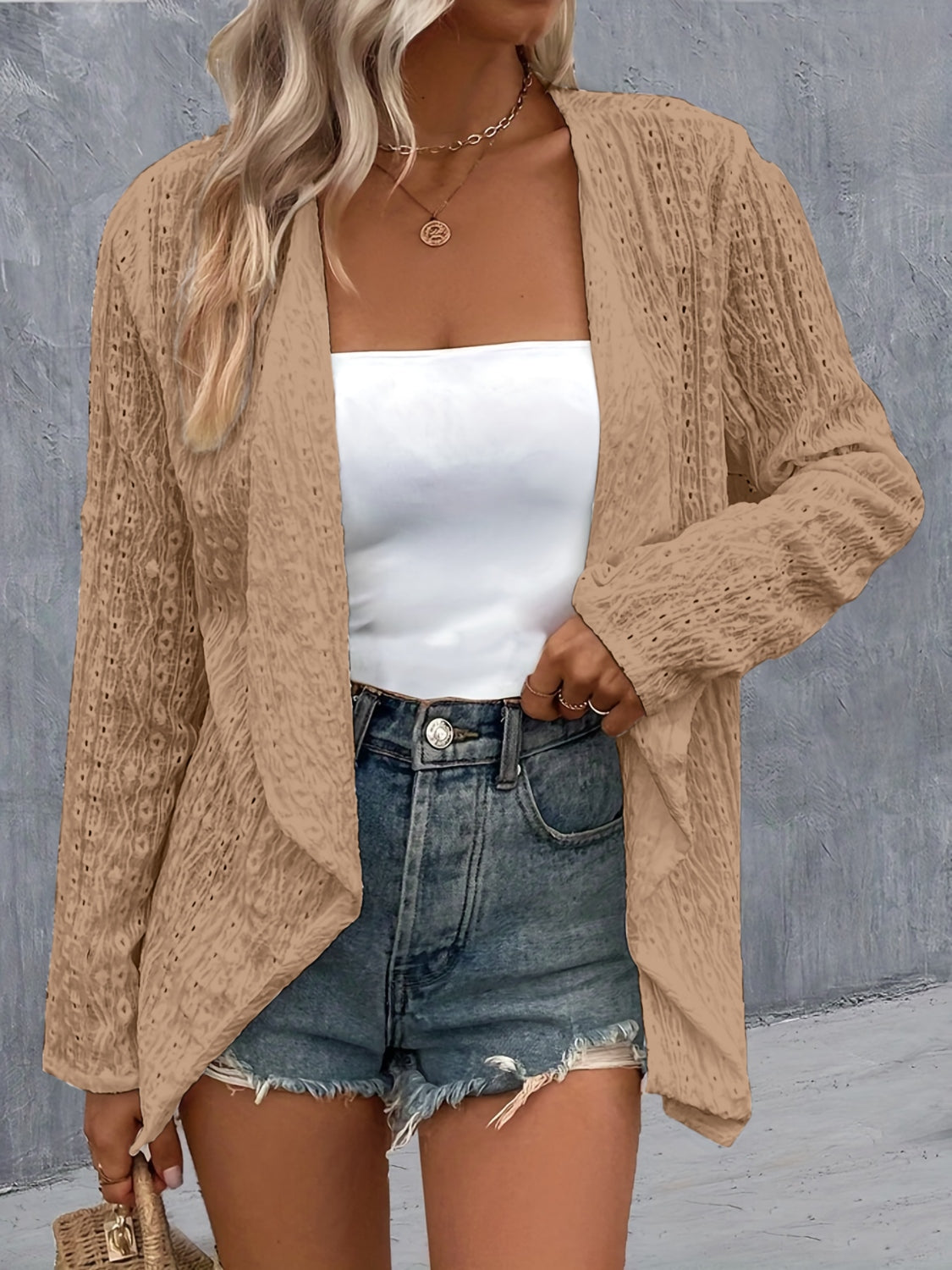Open-weave camel cardigan with draped front and long sleeves, styled with a white tube top and denim shorts.