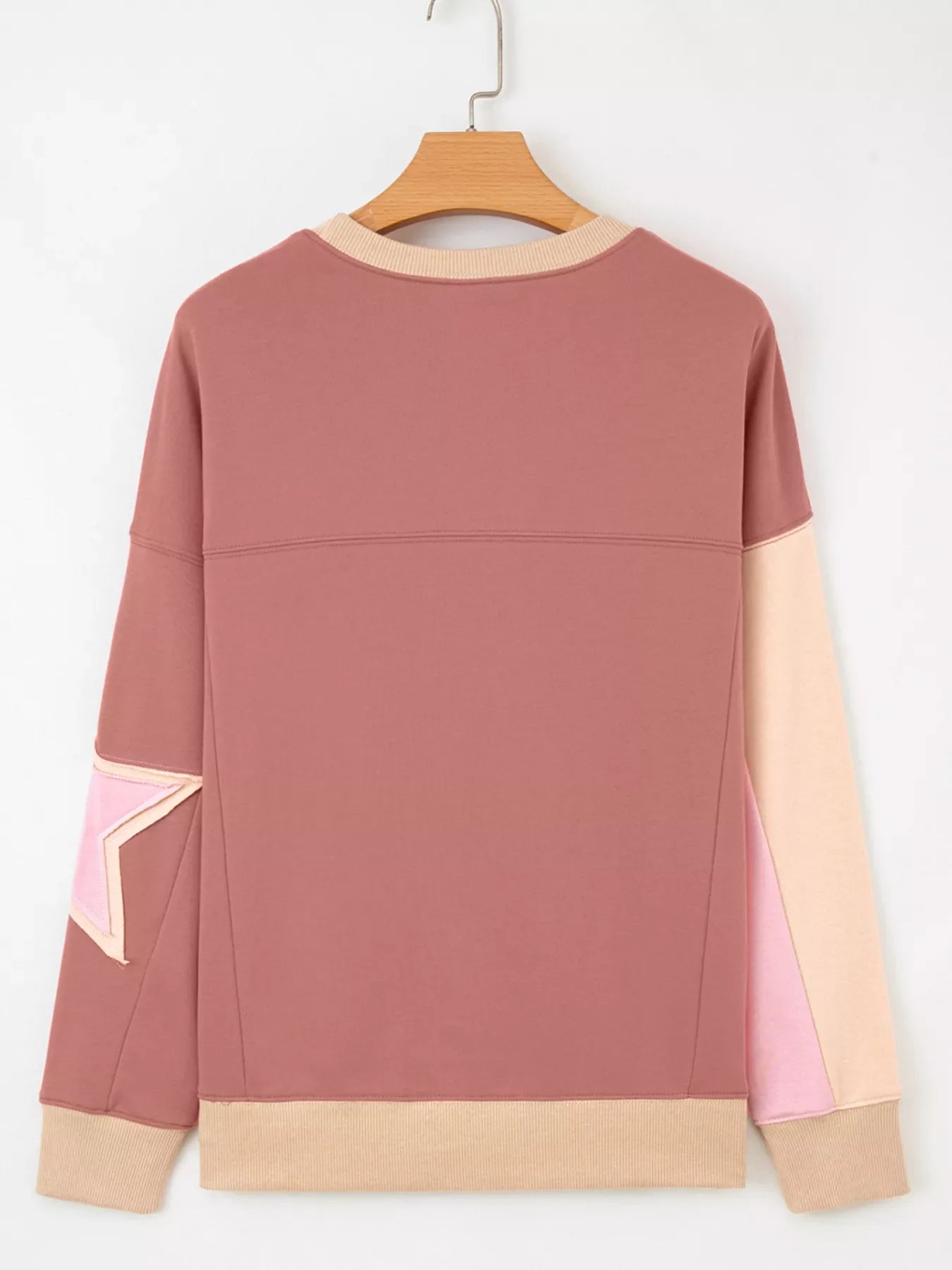 Dusty pink sweatshirt with star patchwork detail, contrast stitching, and ribbed cuffs and hem.