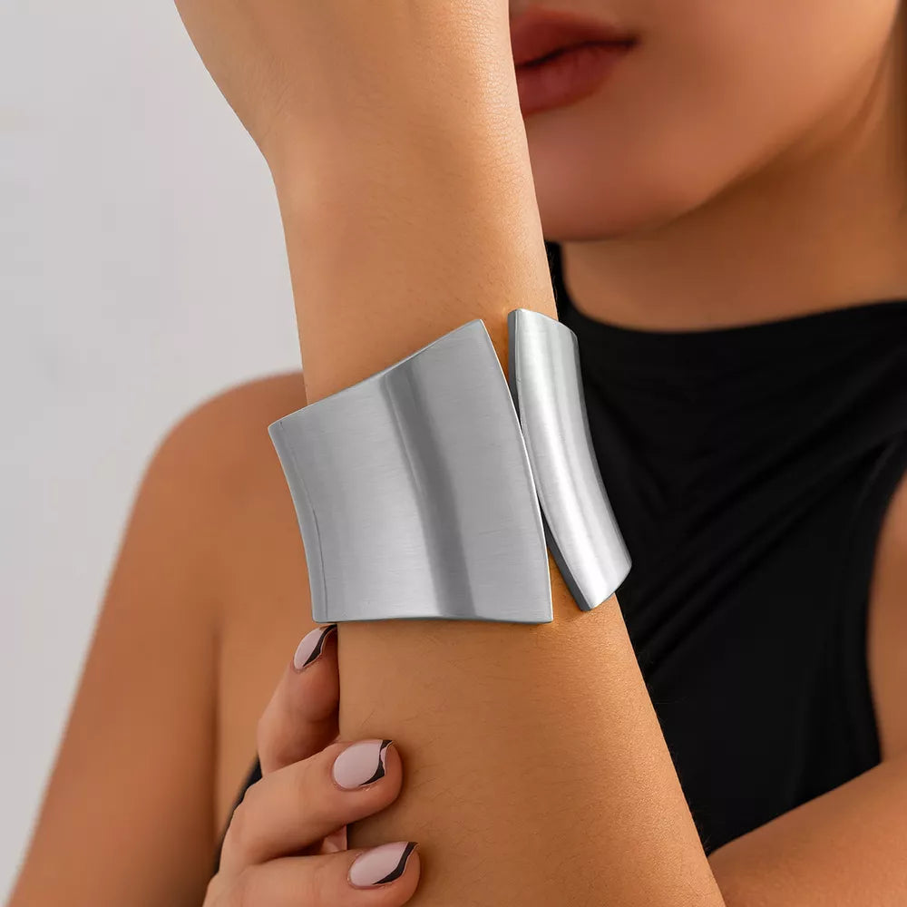 Sculptural silver-toned cuff bracelet with a brushed metal finish and open design.
