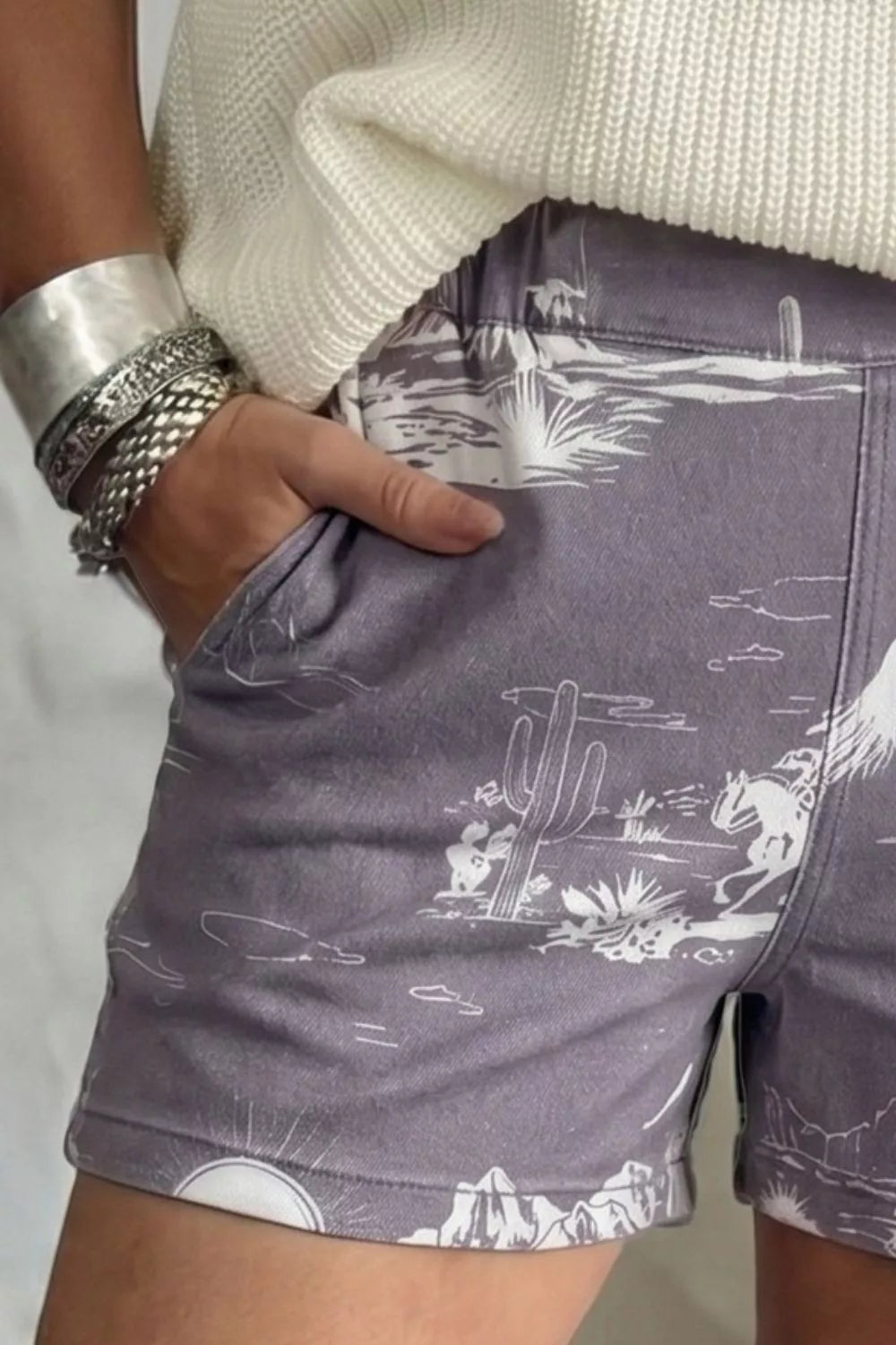 Denim shorts with western desert print, cacti, mountains and cowboy on horse.