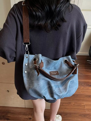 Blue canvas-like slouchy crossbody bag with adjustable strap and brown leather trim.