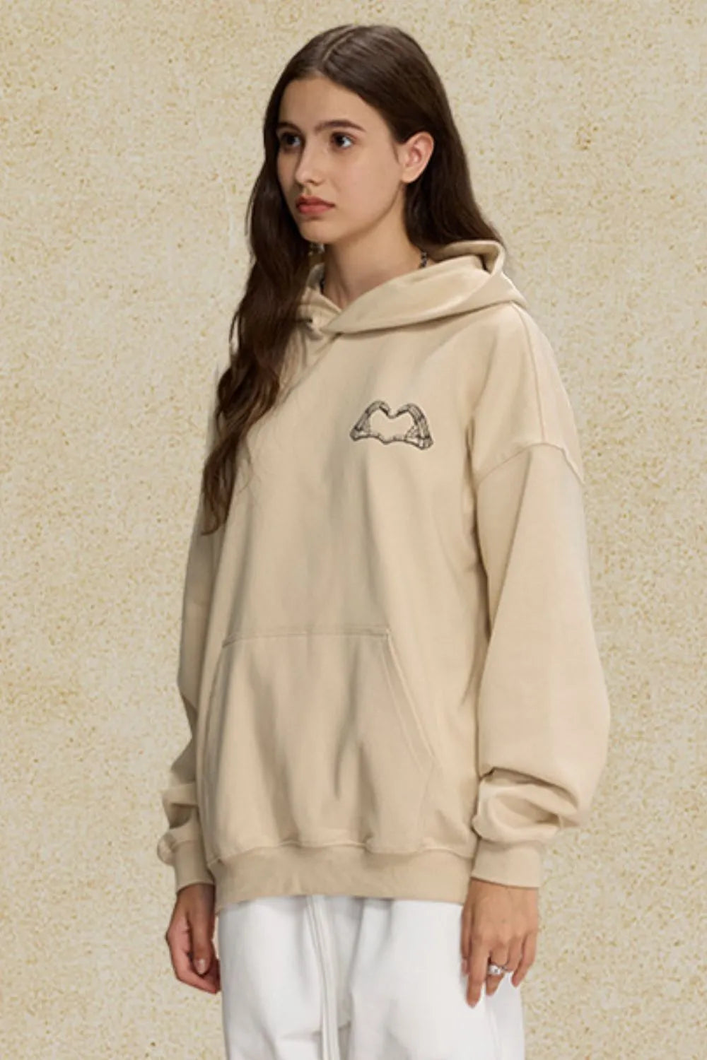 Beige oversized hoodie with embroidered heartbeat chest detail and front pocket.