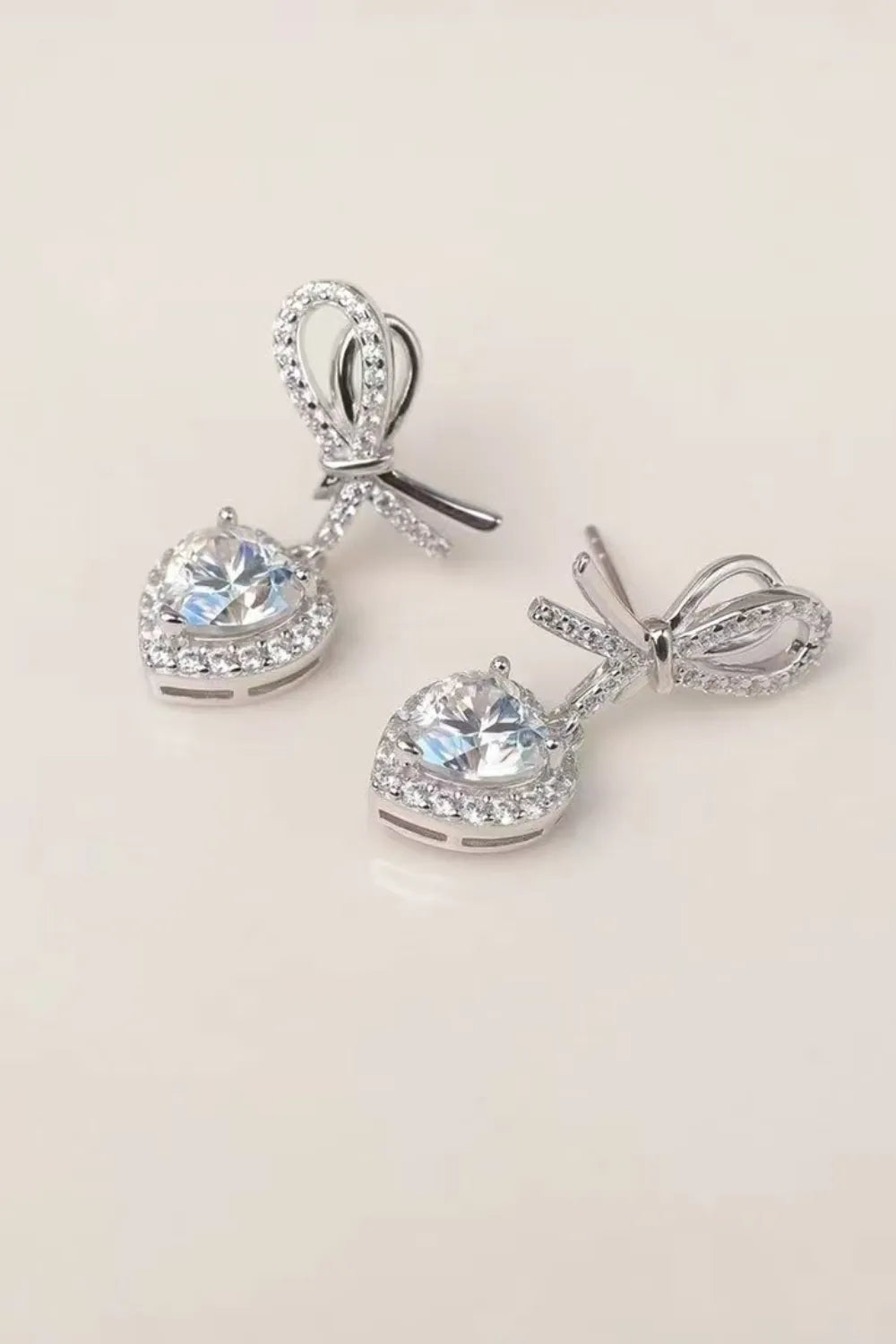 Silver bow-adorned heart moissanite drop earrings with pavé accents.