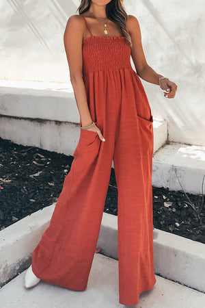 Orange-red smocked bodice palazzo jumpsuit with spaghetti straps and wide legs.