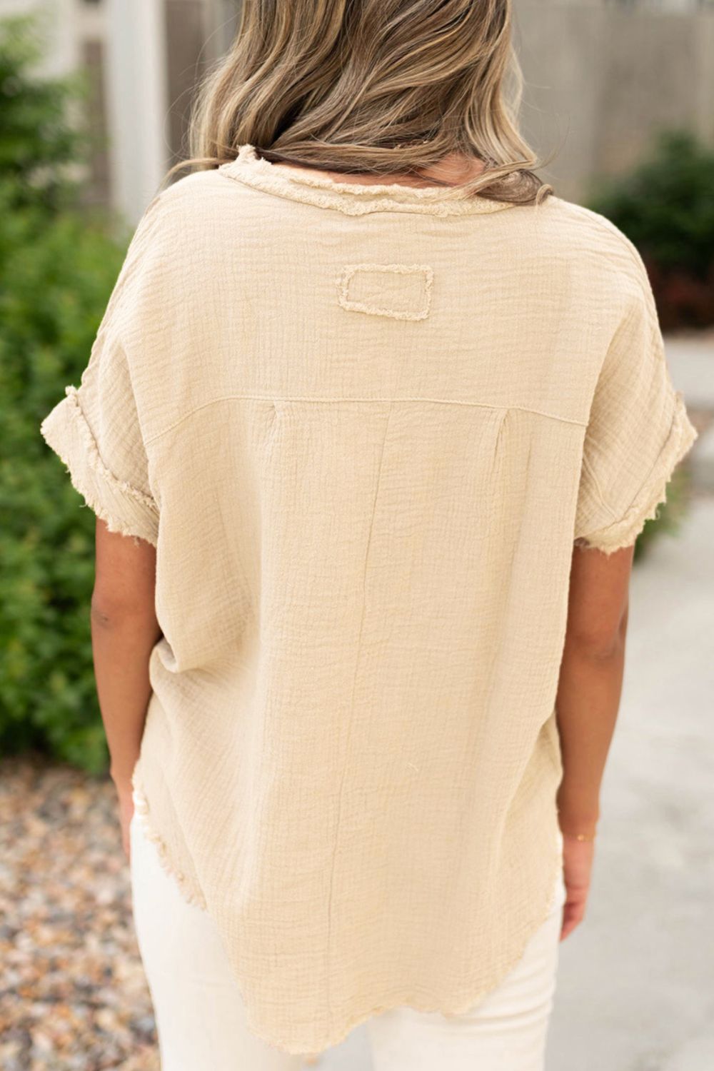 Beige textured gauze henley blouse with raw edges and short sleeves.