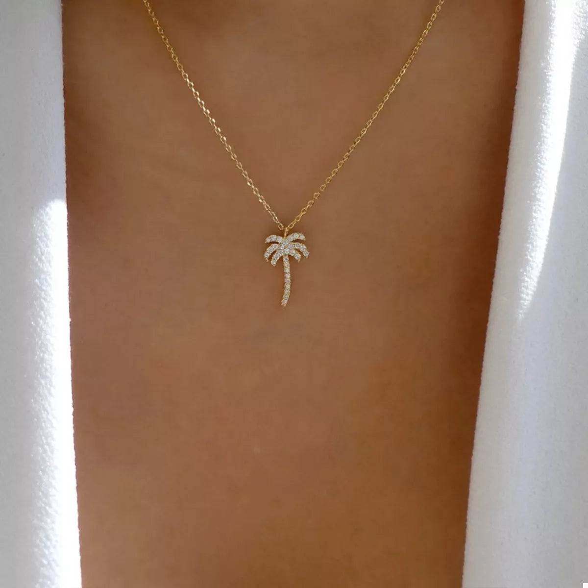 Gold palm tree pendant necklace with pave crystal details on a delicate chain.