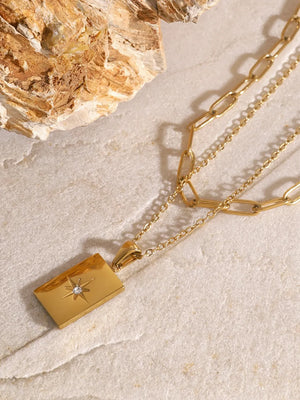 Gold layered chain necklace with rectangular celestial pendant and starburst detail.