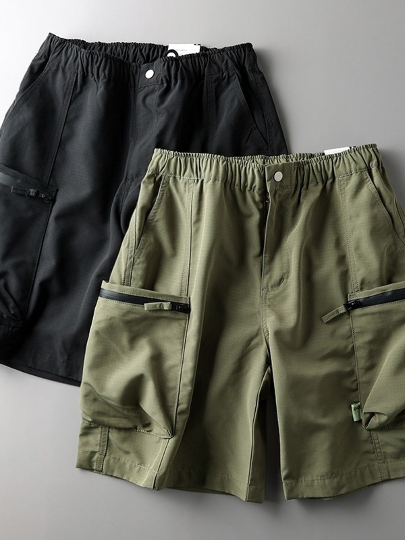 Relaxed fit cargo shorts in green and black with multiple zip pockets and elastic waistband.