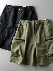 Relaxed fit cargo shorts in green and black with multiple zip pockets and elastic waistband.
