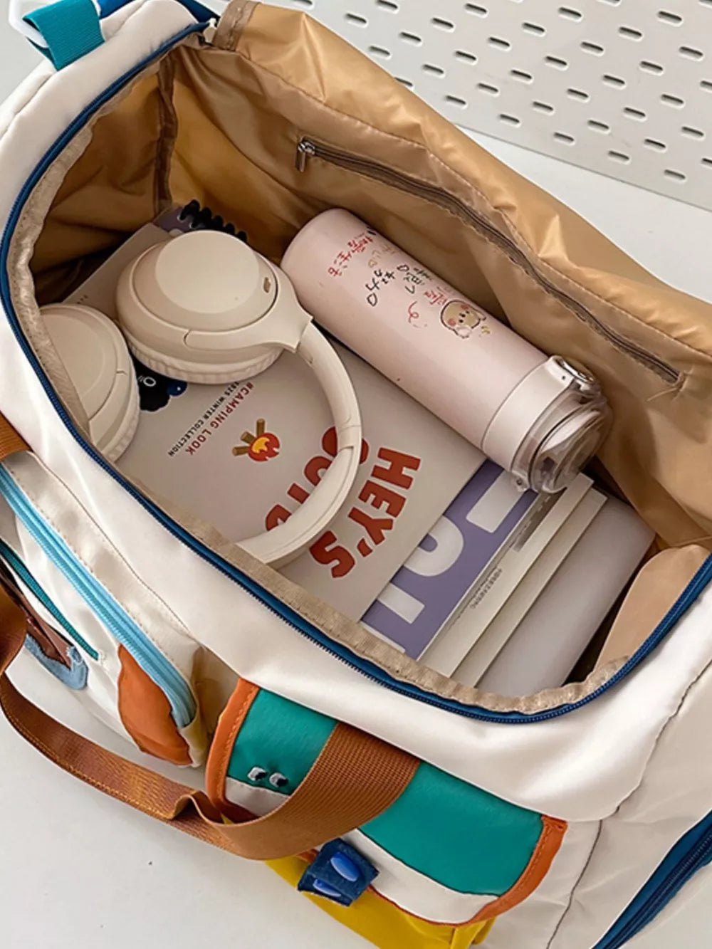 Vibrant multi-pocket nylon travel bag with color block details, shown packed with headphones and a water bottle.