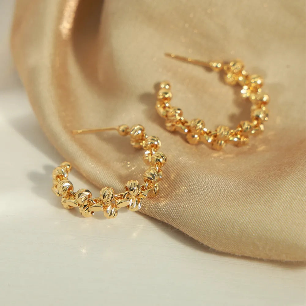 Gold textured orb C-hoop earrings with a beaded, floral-like design.