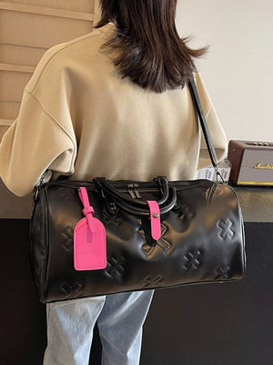 Black embossed cross detail luxury duffel bag with pink luggage tag and strap accents.