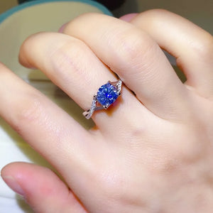 Silver twisted pavé moissanite engagement ring with a blue center stone.