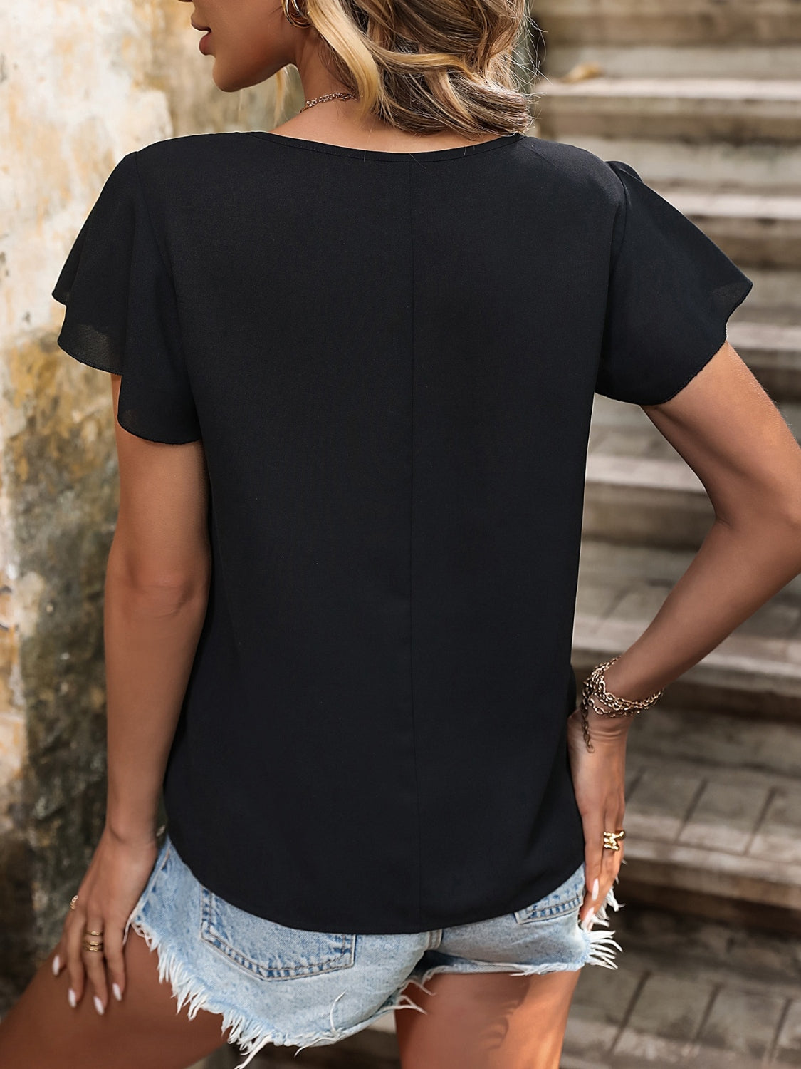 Black asymmetric button-down blouse with flutter sleeves and a casual cut.