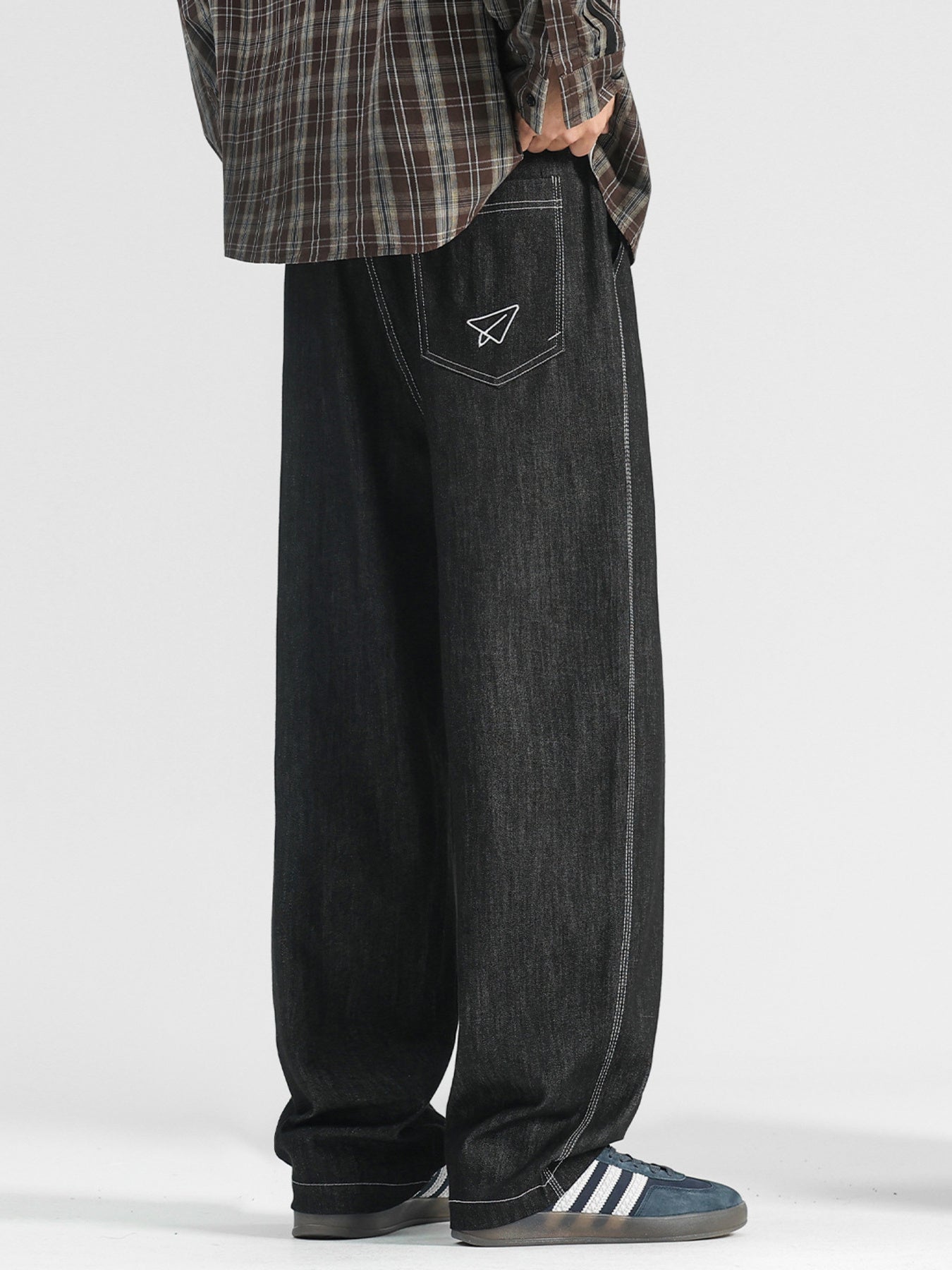 Men's black wide-leg jeans with paper airplane pocket detail and contrast stitching.