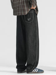 Men's black wide-leg jeans with paper airplane pocket detail and contrast stitching.