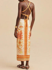 Backless maxi dress with floral print, orange and cream colors, and crisscross straps.