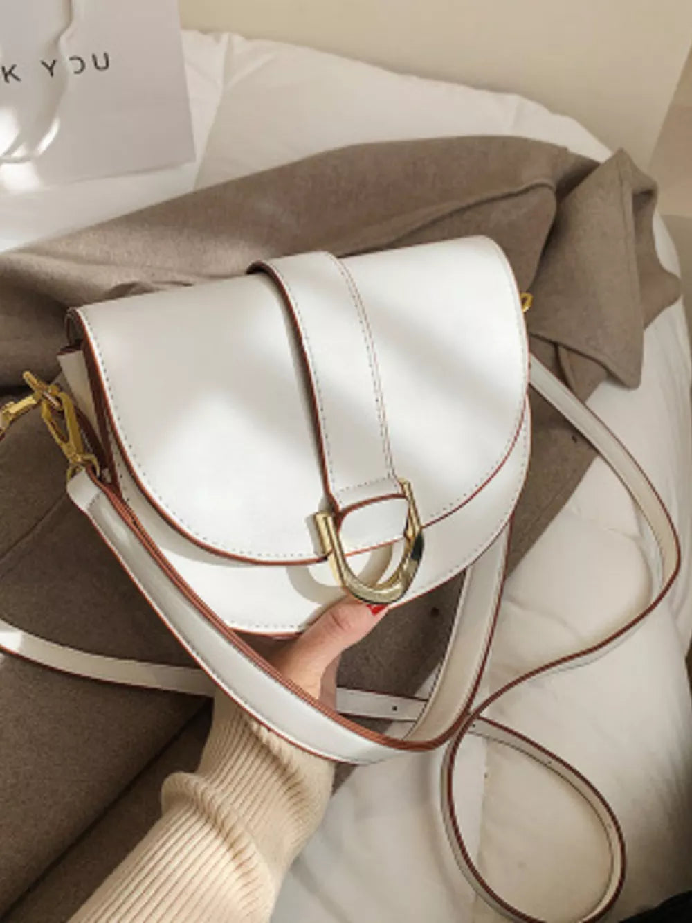 Chic white semi-circular flap crossbody bag with gold buckle detail.