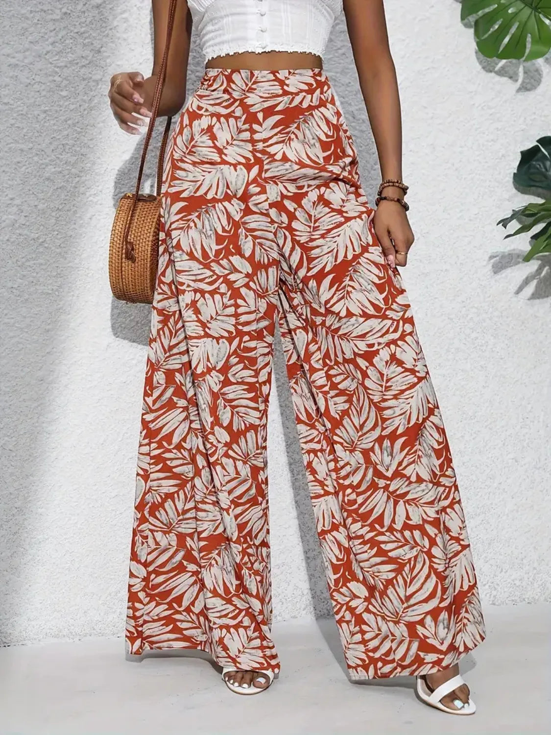 Orange-red palazzo trousers with a tropical leaf print in white and grey, made of 100% polyester.