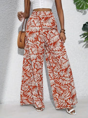 Orange-red palazzo trousers with a tropical leaf print in white and grey, made of 100% polyester.