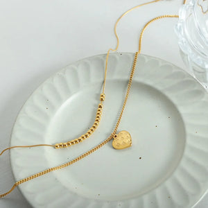 Gold layered necklace with beaded chain and checkered heart charm