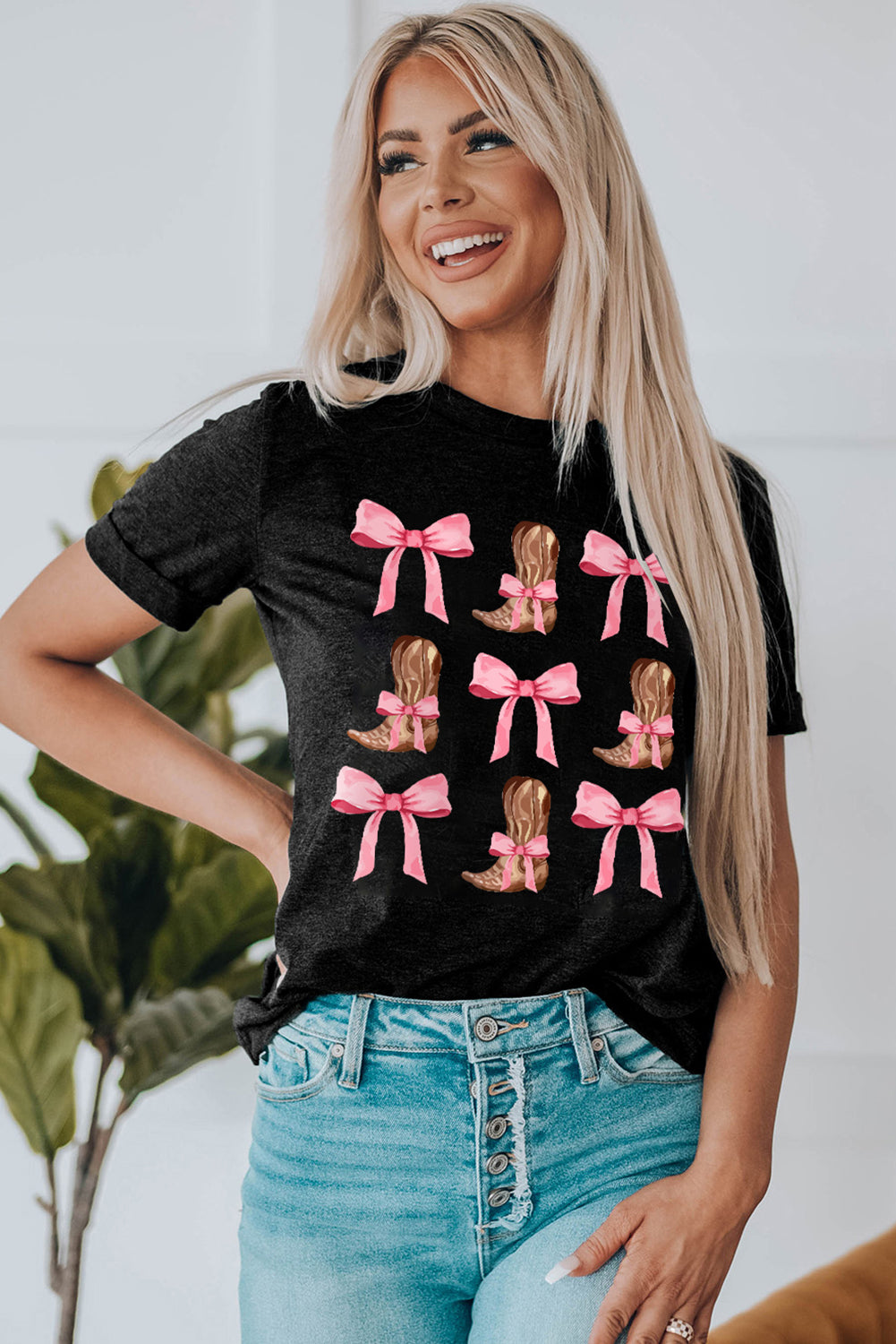 Black t-shirt with a graphic print of brown cowboy boots with pink bows.
