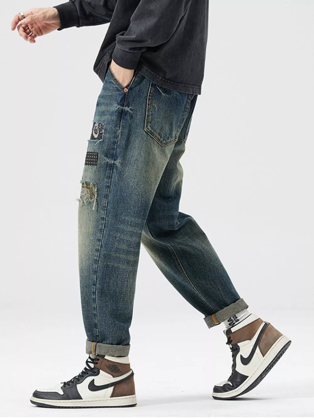 Men's blue distressed cotton jeans with patchwork details and rolled cuffs.