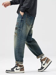 Men's blue distressed cotton jeans with patchwork details and rolled cuffs.