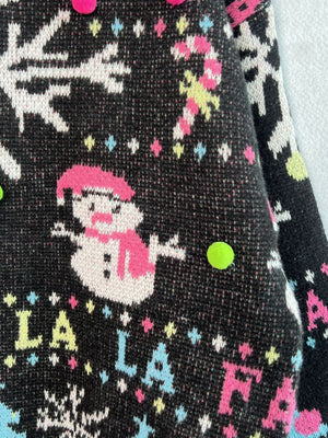 Black knit sweater with snowman, candy cane, and snowflake pattern, embellished with pom-poms.