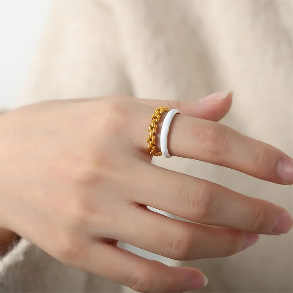 Gold chain link and white enamel open rings stacked on a finger.
