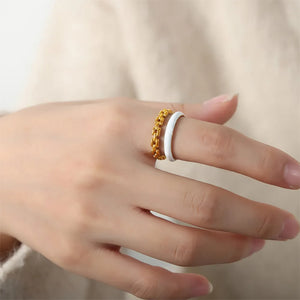 Gold chain link and white enamel open rings stacked on a finger.