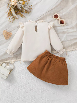 Baby girl's cream ruffle trim top with long sleeves and brown corduroy heart skirt.