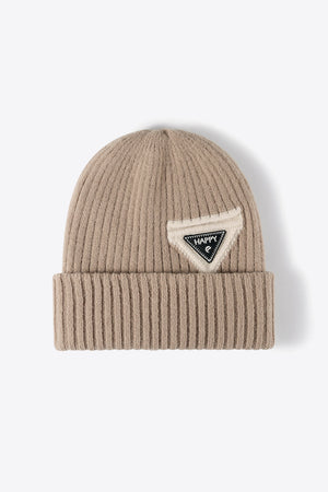 Beige ribbed acrylic beanie with a triangular patch that says HAPPY