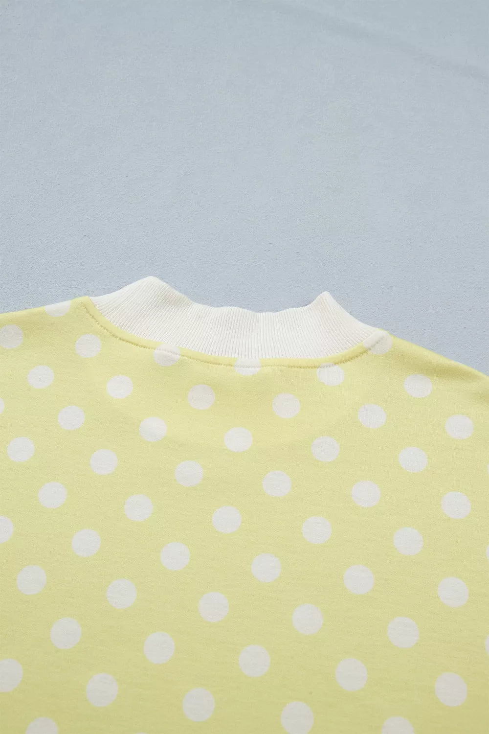 Pastel yellow polka dot polyester top with white ribbed neckline.