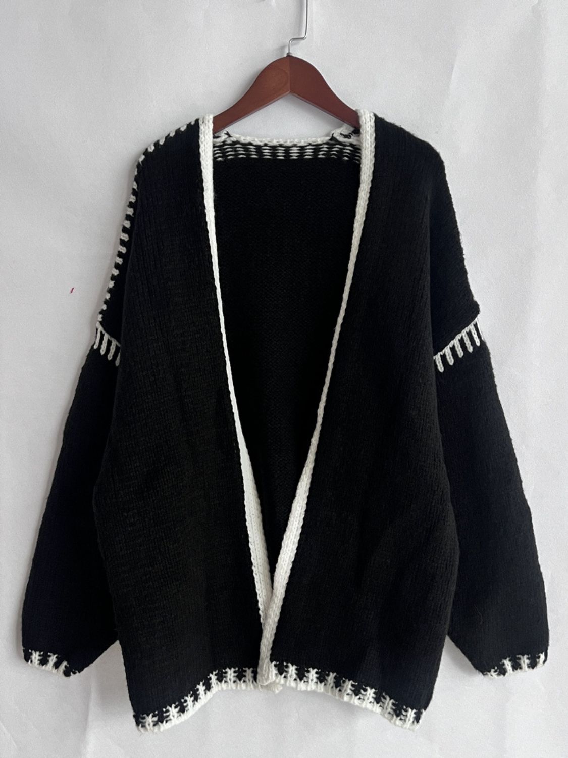 Black oversized knit cardigan with white contrast stitching detail on edges and sleeves.