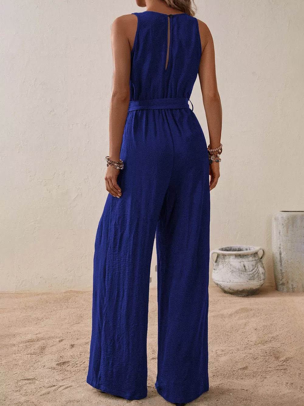 Royal blue V-neck tie-waist wide-leg romper with textured fabric and button closure at back neck.